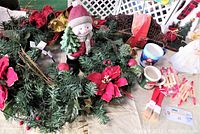 Photo showing artificial wreath with red poinsettias, ceramic snowman figurine in red hat and scarf, various greenery and Christmas decorations on table