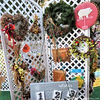 Photo showing a selection of floral wreaths hanging on white lattice. Varied styles including natural dried floral wreaths, green foliage wreath, and one with a red ribbon bow.