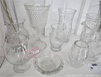 Clear glass vases, pitcher and ashtrays displayed together on white shelf surface, various sizes and styles