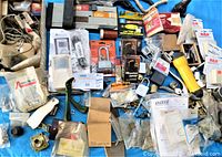 Full overview of the lot showing multiple padlocks, hardware parts, cables, vintage green Gumby figurine, and other assorted electrical and plumbing components spread out on a blue surface.