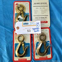 Four solid bronze snap hooks, three sealed in original packaging, one package opened, laid on blue fabric background.
