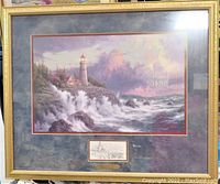 Full view of the framed Thomas Kinkade "Conquering the Storms" lithograph print showing the coastal scene with lighthouse and stormy ocean.
