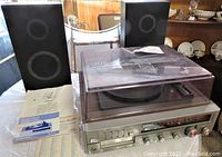 Wide view of Emerson stereo receiver system with record changer under dust cover, two black speakers, and printed documents on table.
