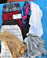Nine vintage women's scarfs arranged flat on a blue background showing various colors and textures, including solid colors, plaid, and multicolor patterns.
