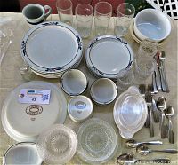 Overview of entire lot showing Dansk plates and bowls stacked, drinking glasses, covered glass dish, and flatware placed on table.