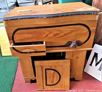 Front angled view of wooden cabinet showing open top lid, partially open drawer with damage, and lower door panel with black painted outline and letter 'D'.
