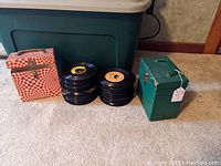 Overview photo showing the two 45 record carriers and several stacks of 45 RPM vinyl records on carpet in front of a storage bin.