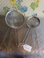 Two metal kitchen sieves placed side by side showing comparative sizes and fine mesh screens.