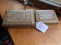 Two rectangular vintage wooden boxes with mother of pearl inlay on a wooden surface, one larger and one smaller