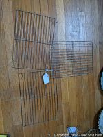 Three rectangular metal cooling racks arranged on a wooden floor, photographed to show the full set.