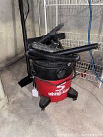 Front side view of the red 5 gallon Shop-Vac wet/dry vacuum with black hose and floor nozzle attached.