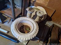 Wide angle photo showing the large urn planter and two bird bath pedestals placed on floor with leaf debris inside planter.