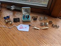 Full collection of assorted men's cufflinks and tie accessories displayed on wooden surface including Swank boxed cufflinks and several pairs with metal and enamel finishes.