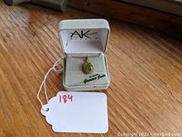 Full view of the costume jewelry necklace pendant in its original soft jewelry box on a wooden surface, with a white lot tag visible.