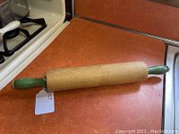Rolling pin with green handles angled on orange countertop showing natural wood barrel and green handles.