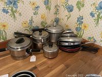 Full lot of vintage stainless steel cookware displayed on countertop, showing various saucepans, double boiler, and pressure cooker.