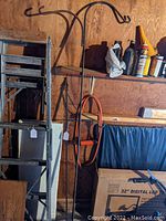Full view of both wrought iron planter hangers leaning against a wooden wall beside other items