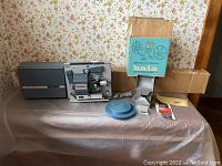 Full lot of vintage Super 8 movie equipment including projector, editor, screen, reels and manuals displayed on a table.