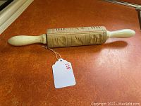 Top angle view of the vintage cookie rolling pin laid on orange countertop, showing the carved rolling surface and white handles.