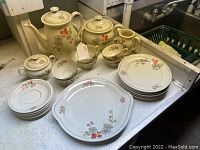 Full view of the tea and coffee set items arranged on the countertop, showing pots, cups, saucers, plates, sugar bowl, and creamer with floral design.