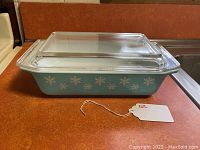 Side angle of blue Pyrex rectangular casserole dish with white snowflake patterns and clear lid in very good condition
