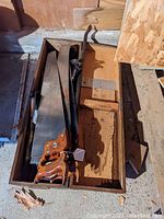 Wooden tool chest with three hand saws visible, showing their wooden handles with decorative engraving and metal blades