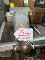 Close-up of the metal bench vise mounted on a workbench with a label indicating price and condition.