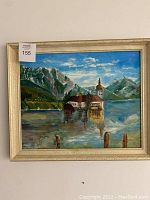 Full view of the framed acrylic painting showing the mountain lake scene with buildings, water reflections, and mountains in the background.