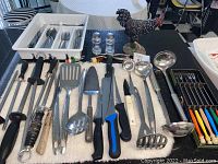 Wide view of the collection laid out on table showing all items including knives, sharpening steels, utensils, salt and pepper shakers, and rooster figurine