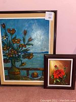 Image showing two framed floral paintings next to a pink wall, one larger with orange flowers and one smaller with red roses.