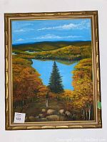 Full view of the framed nature scene painting showing lake, hills, and autumn trees within a gold bamboo-styled frame.