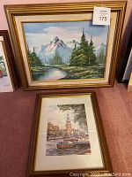 Two framed art pieces leaning against a wall: top landscape and bottom Amsterdam scene with boats and tower