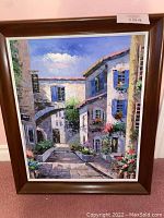 Full view of framed painting showing village street with buildings, stairs, flowers, and blue sky.