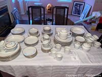 Full set of Kahla gold band white scalloped dinnerware spread on table with cups, saucers, plates, creamer, sugar bowl, and serving dishes.