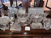 Wide view of all crystal serving pieces arranged on table, showing variety including bowls, trays, decanter, lidded dishes, and salt/pepper shakers.