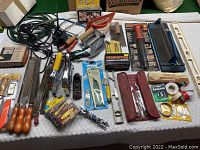 Overview of miscellaneous hand and masonry tools spread on table, including staple guns, hammers, files, and fasteners.