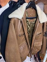 Three jackets hanging, showing the brown leather jacket with shearling collar in front and two blazers behind it.