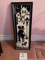 Framed black and cream needlepoint artwork showing a couple standing by a street lamp, full framed view.