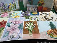 Collection of original watercolor paintings of flowers and still life on table.