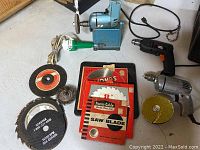 Shows power tools including two corded drills, a blue bench-mounted grinder, various cutting and grinding discs, and wire brushes.