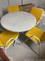 Photo showing round metal table with four stackable chairs with yellow cushions arranged around it.
