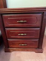 Front view of first nightstand showing three drawers and carved side column