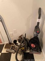 Photo showing vintage Filter Queen metal cylinder vacuum cleaner with hose and attachments along with Hoover upright vacuum cleaner.