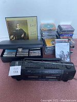 Full view of black Pulser stereo cassette player with carrying case containing cassette tapes, piles of CDs, and vinyl records behind.