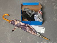 Photo showing boots, socks and umbrella inside a box and placed on the floor.