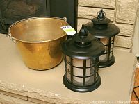 Brass bucket alongside pair of black metal lantern candleholders with battery candles.