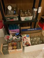 Overview of shelving unit with several boxes and jars on and under it, including Bernardin jars, pickling kit box, and the preserving guide book.