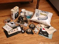 Complete cat-themed assortment showing pillow, mugs, figurines, towels, hooks, and tin arranged on floor