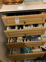 Four partially open wooden drawers showing organized kitchen cutlery trays with stainless steel utensils and various kitchen tools scattered in some drawers, some wrapped or boxed items visible on side.