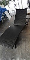 Front view of black plastic rattan folding deck lounger showing curved ergonomic design.